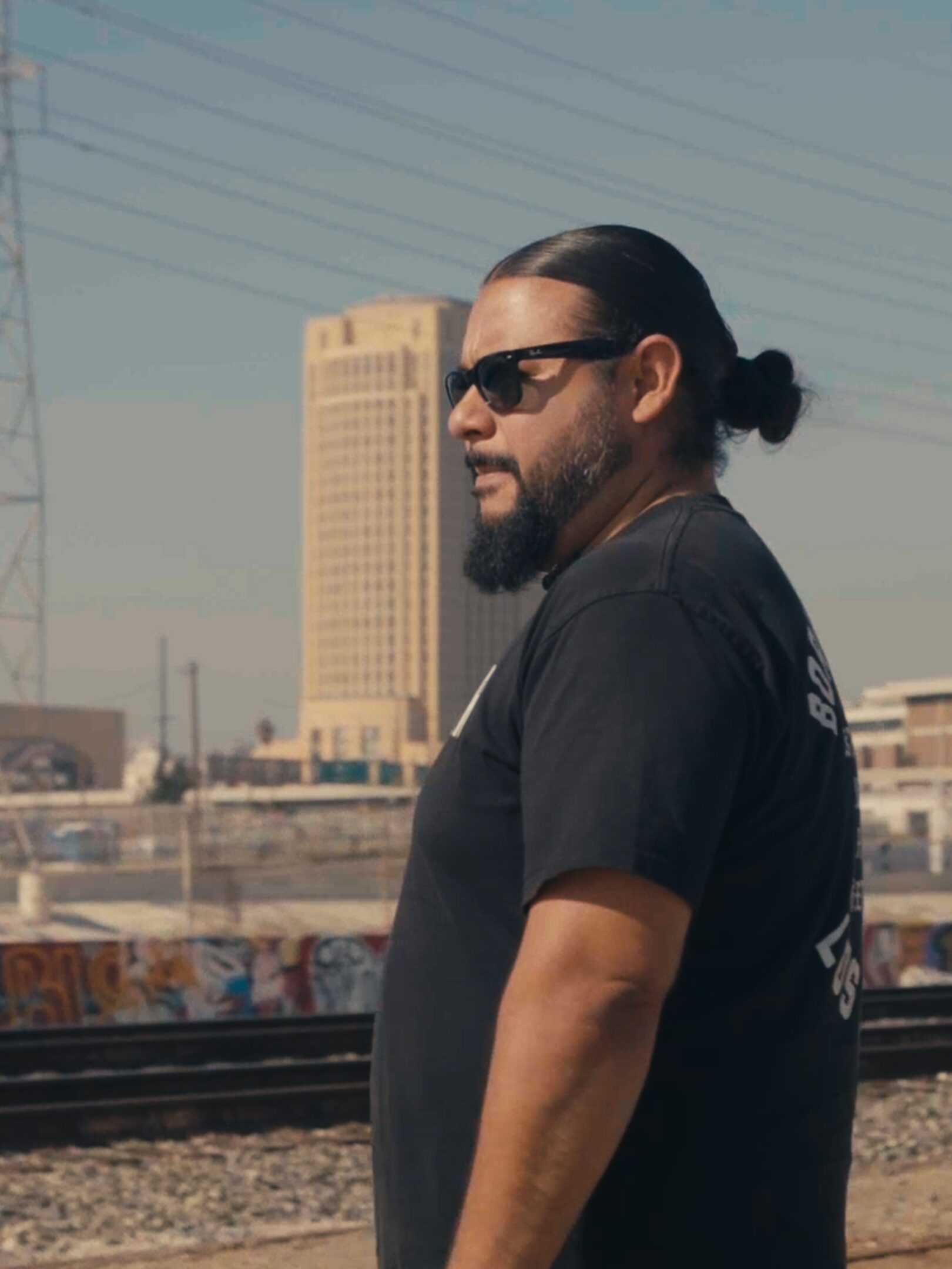 mark, standing in profile, in front of a city skyline as a freight train passes by.
